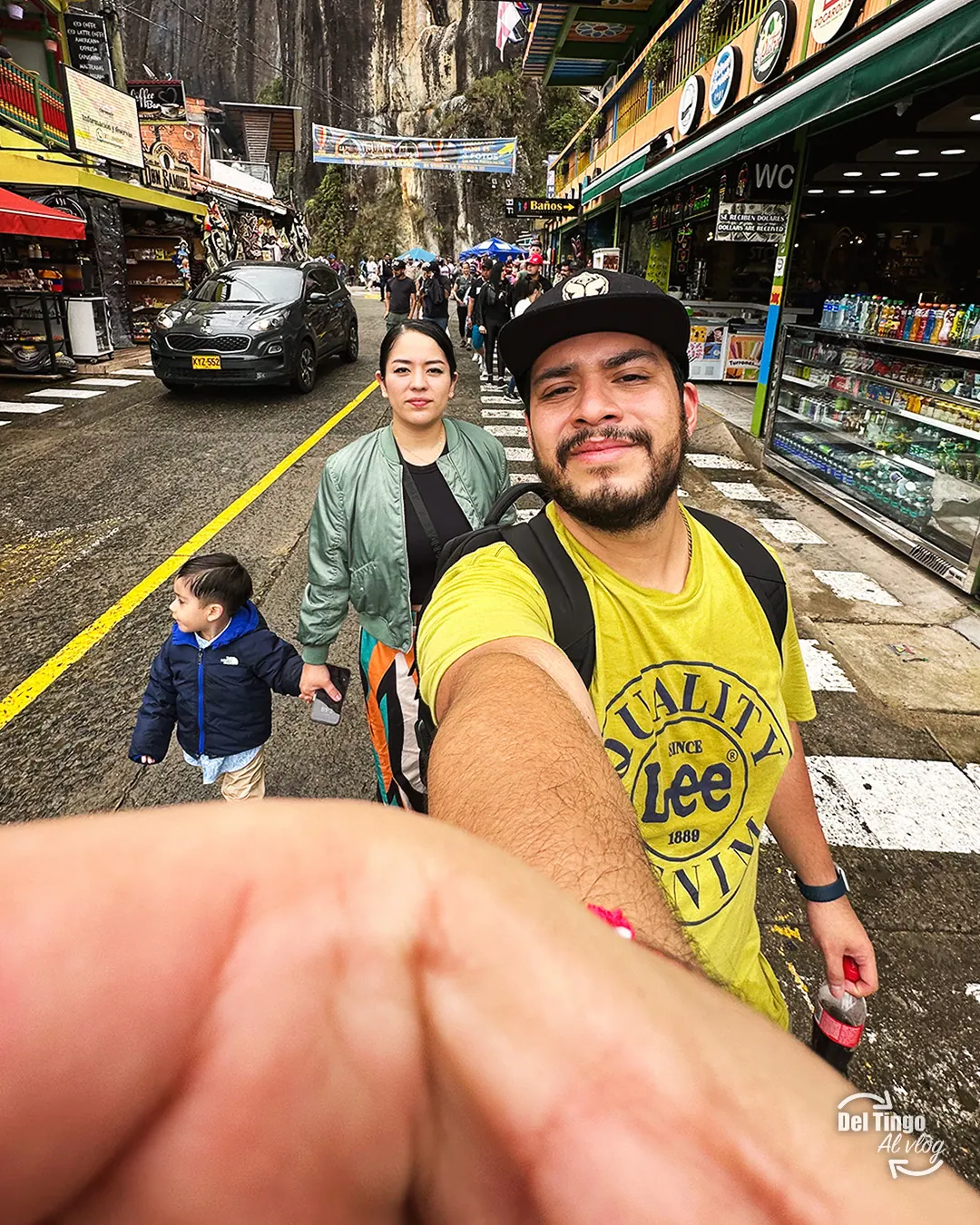 Selfie de la familia cruzando la calle al pie de la Piedra del Peñol: papá con playera amarilla, mamá con chamarra verde y Sebastián con chamarra azul de la mano