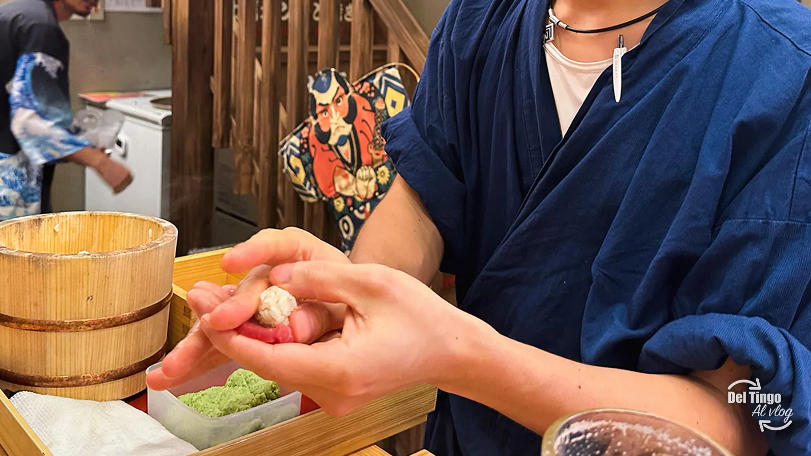 El itamae con yukata azul formando el nigiri en la barra, a treinta centímetros de ti