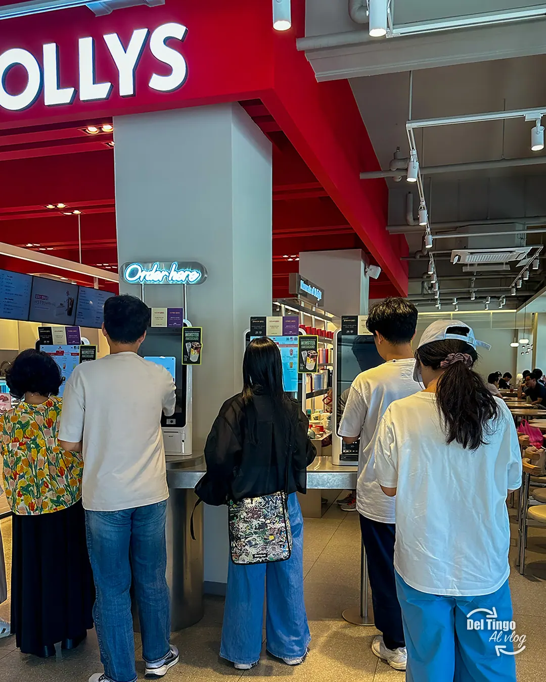 Clientes formados frente a los kioscos de auto-pedido de una sucursal de Hollys Coffee en Seúl, con un letrero de neón Order here arriba
