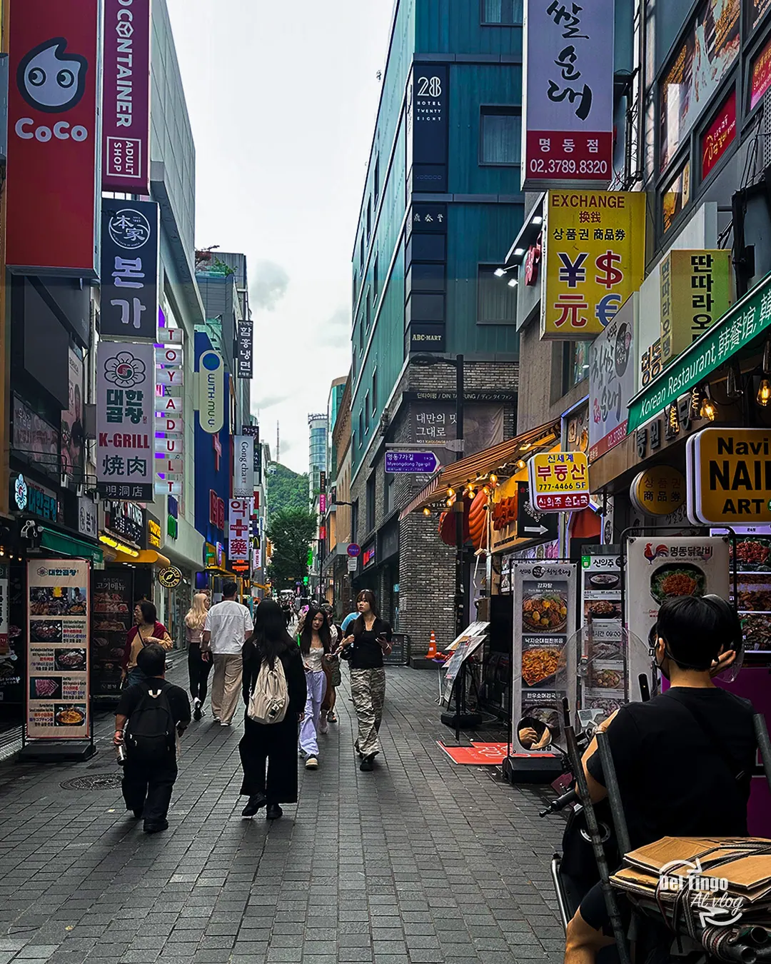 Calle peatonal de Myeongdong en Seúl llena de letreros coreanos de restaurantes, casas de cambio y tiendas, con peatones recorriéndola