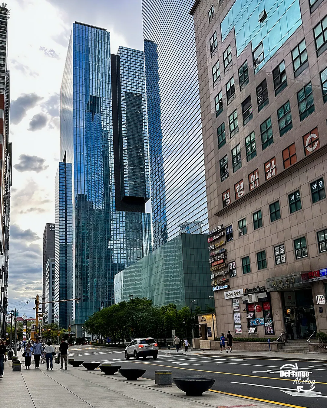 Calle del distrito de Gangnam en Seúl con sus rascacielos de cristal, un edificio comercial lleno de letreros coreanos y autos pasando por el cruce peatonal