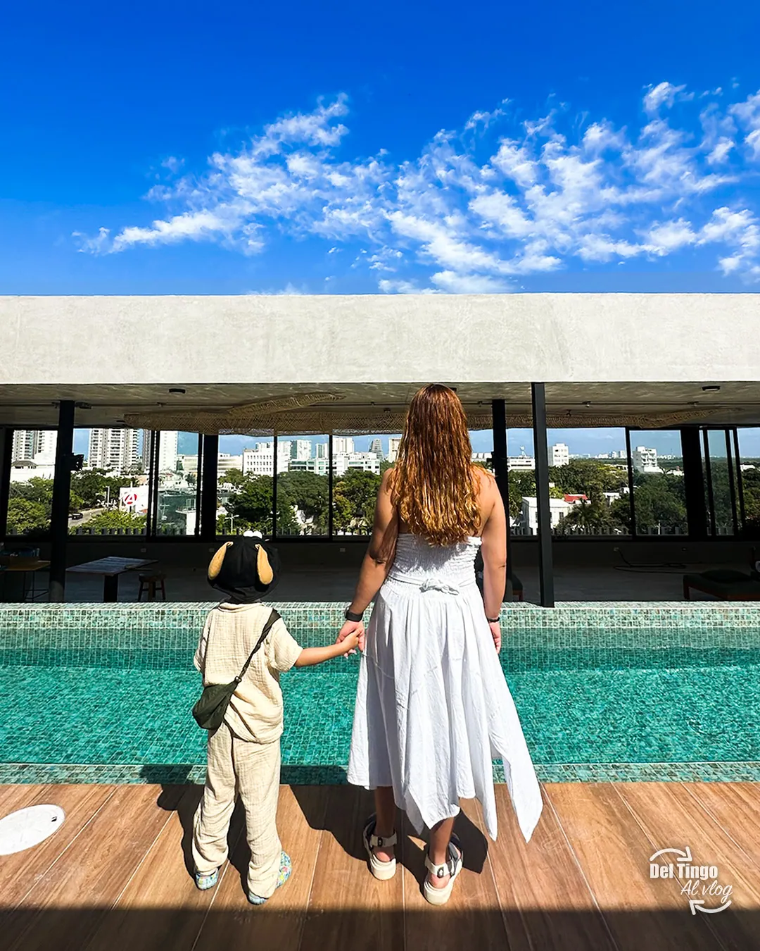 Madre y niño tomados de la mano de espaldas en el rooftop del hotel en Cancún, viendo la ciudad bajo un cielo azul